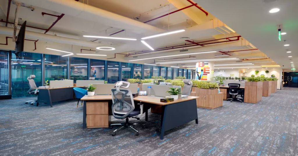 A modern open-office space with wooden desks, ergonomic chairs, indoor plants, and vibrant decor.